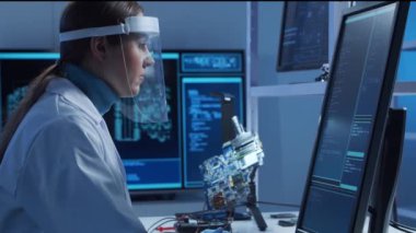 Kadın mikro elektronik mühendisi, bilgisayar sistemleri ve mikroişlemciler üzerine modern bir bilim laboratuvarında çalışıyor. Elektronik fabrika işçisi ana kartı test ediyor ve yazılımı kodluyor..