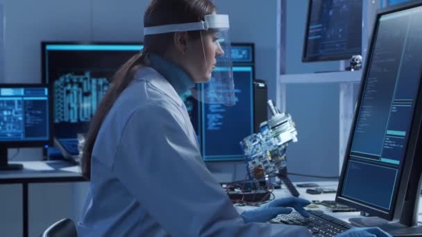 女性のマイクロエレクトロニクスエンジニアは、コンピューティングシステムとマイクロプロセッサに関する現代の科学研究室で働いています。電子工場労働者はマザーボードをテストし、ファームウェアをコーディングしています. — ストック動画