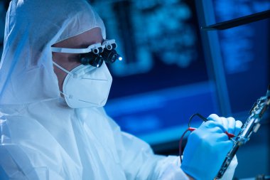 Mikro elektronik mühendisi, bilgisayar sistemleri ve mikroişlemciler üzerine modern bir bilim laboratuvarında çalışıyor. Koruyucu giysili profesyonel elektronik fabrika işçisi ana kartı test ediyor ve yazılımı kodluyor..