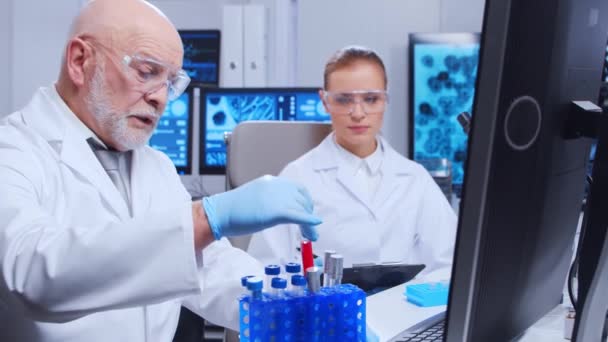 Oudere hoogleraar en jonge laboratoriumassistent doen wetenschappelijk experiment in een modern laboratorium. Genetische ingenieurs werkplek. Het concept van wetenschap, geneeskunde en vaccinontwikkeling. — Stockvideo