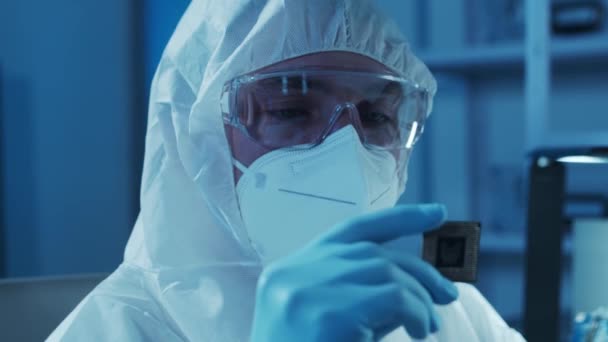 Microelectronics engineer works in a modern scientific laboratory on computing systems. Electronic factory worker in a protective suit is looking on the microprocessor. — Stock Video