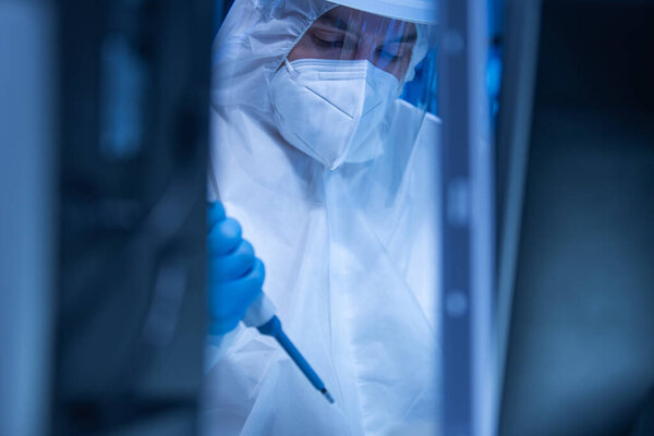 Врач в защитном костюме проводит научные эксперименты и разрабатывает вакцину в современной лаборатории. Рабочее место инженеров-генетиков. Концепция науки и медицины.