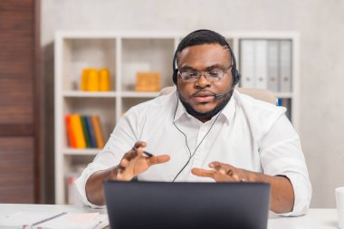 Serbest Çalışan 'ın işyeri. Afro-Amerikalı adam merkez ofiste bilgisayar, kulaklık ve diğer cihazları kullanarak çalışıyor. Eleman konferans görüşmesi yapıyor. Uzak görev.