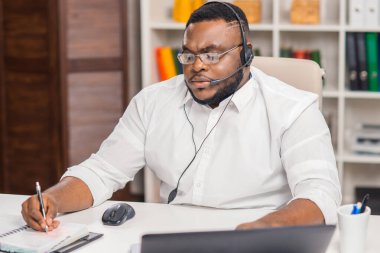 Serbest Çalışan 'ın işyeri. Afro-Amerikalı adam merkez ofiste bilgisayar, kulaklık ve diğer cihazları kullanarak çalışıyor. Eleman konferans görüşmesi yapıyor. Uzak görev.