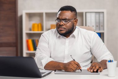 Ev ofisinde serbest tasarımcı işyeri. Genç Afro-Amerikalı bir adam bilgisayar, grafik tableti ve diğer cihazları kullanıyor. Uzak görev.