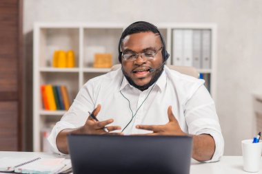 Serbest Çalışan 'ın işyeri. Afro-Amerikalı adam merkez ofiste bilgisayar, kulaklık ve diğer cihazları kullanarak çalışıyor. Eleman konferans görüşmesi yapıyor. Uzak görev.