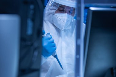 Koruyucu kıyafetli doktor modern bir laboratuvarda bilimsel deneyler yapıyor ve aşı geliştiriyor. Genetik mühendisliği işyeri. Bilim ve tıp kavramı.