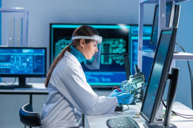 Kadın mikro elektronik mühendisi, bilgisayar sistemleri ve mikroişlemciler üzerine modern bir bilim laboratuvarında çalışıyor. Profesyonel elektronik fabrika işçisi ana kartı test ediyor ve yazılımı kodluyor..