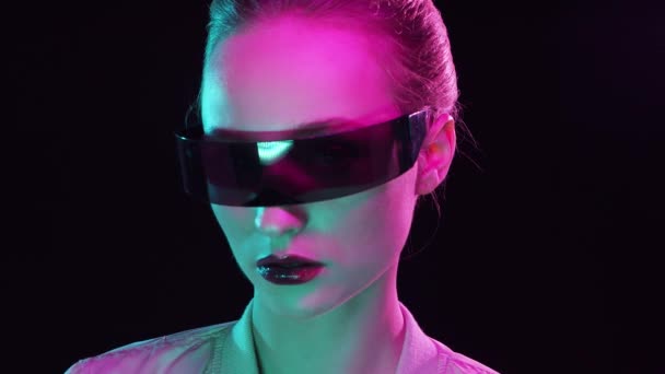 Siber punk tarzında genç bir kızın portresi. Gelecekteki güneş gözlükleriyle poz veren genç bir kadın. Yaratıcı stüdyo ışığı. — Stok video