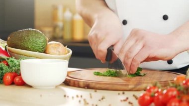 Genç aşçı modern bir mutfakta bitki ve maydanoz kesiyor. Adam evde yemek hazırlıyor. Sağlıklı yemek pişirmek..
