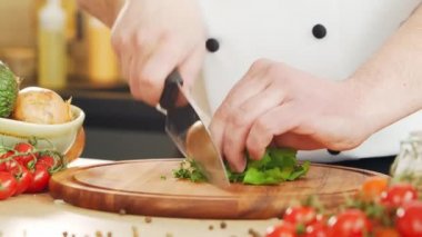 Genç aşçı modern bir mutfakta bitki ve maydanoz kesiyor. Adam evde yemek hazırlıyor. Sağlıklı yemek pişirmek..