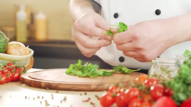 Genç aşçı modern bir mutfakta bitki ve maydanoz kesiyor. Adam evde yemek hazırlıyor. Sağlıklı yemek pişirmek..