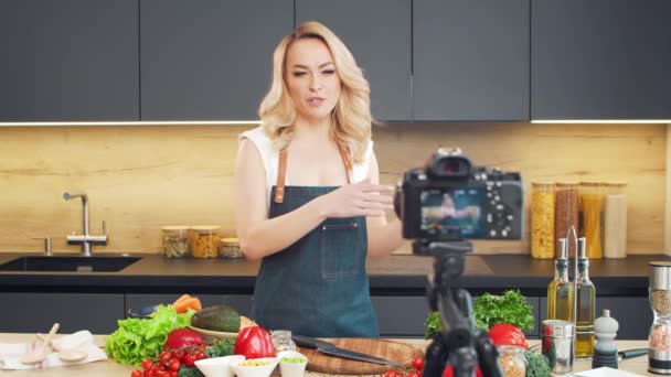 Mujer joven prepara la comida y organiza un espectáculo de cocina. El blogger fluye desde la cocina. Preparación vegetariana de alimentos saludables. — Vídeos de Stock