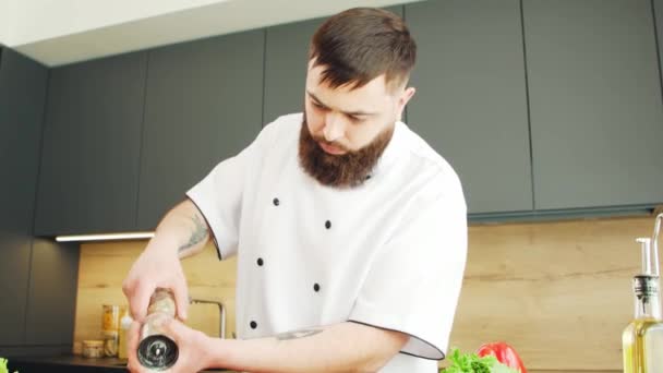 Chef muda pengasinan makanan di dapur modern. Pria itu menyiapkan makanan di rumah. Memasak makanan sehat. — Stok Video