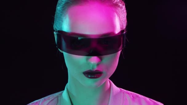 Portrett av tenåringsjente i cyberpunk-stil. En ung kvinne som poserer i futuristiske solbriller. Kreativt studiolys. – stockvideo