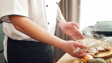 Genç aşçı modern bir mutfakta ızgara biftek hazırlıyor. Adam evde yemek hazırlıyor. Sağlıklı yemek pişirmek..