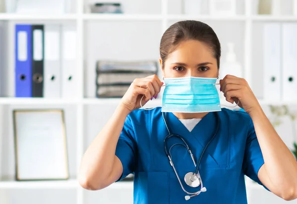 Médico profesional trabajando en consultorio hospitalario, Retrato de joven y atractiva médica en máscara protectora. — Foto de Stock