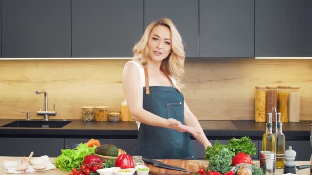 Mujer joven prepara la comida y organiza un espectáculo de cocina. El blogger fluye desde la cocina. Preparación vegetariana de alimentos saludables. — Vídeos de Stock