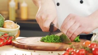 Genç aşçı modern bir mutfakta bitki ve maydanoz kesiyor. Adam evde yemek hazırlıyor. Sağlıklı yemek pişirmek..