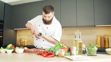 Genç aşçı modern bir mutfakta yiyecek tuzluyor. Adam evde yemek hazırlıyor. Sağlıklı yemek pişirmek..