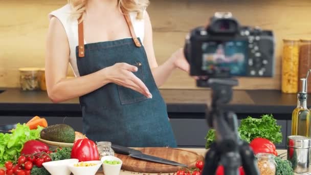 Genç bir kadın yemek hazırlıyor ve bir yemek programı sunuyor. Blogcu mutfaktan yayın yapıyor. Vejetaryen sağlıklı yemek hazırlığı. — Stok video