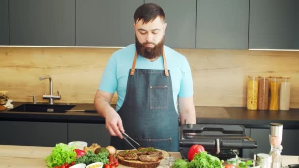 Jovem chef preparando bife de carne grelhada em uma cozinha moderna. O homem prepara comida em casa. Cozinhar alimentos saudáveis. — Vídeo de Stock