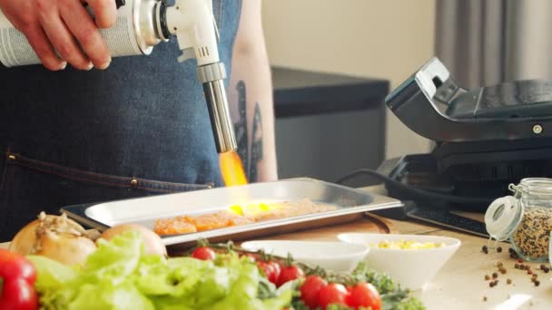 Genç aşçı modern bir mutfakta somon balığını gaz ocağıyla kızartıyor. Adam evde yemek hazırlıyor. Sağlıklı yemek pişirmek.. — Stok video