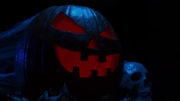 Enge lachende pompoen en een oude schedel op een donkere achtergrond. Halloween, hekserij en magie. — Stockvideo
