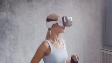 Spor giyimli genç ve sportif kız sanal gerçeklik kaskı kullanarak evde egzersiz yapıyor. Formda ve narin sarışın kadın spor ve spor için geliyor. Sağlık sigortası, yağ yakma ve sağlık..