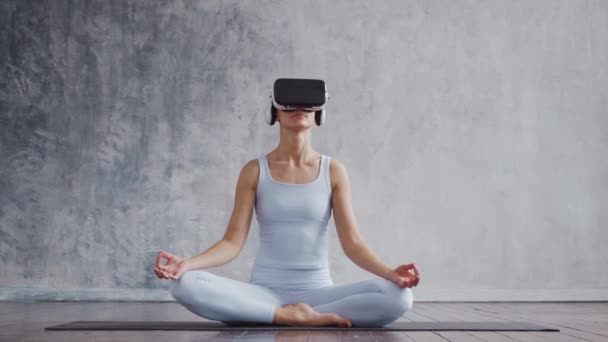 Chica joven y deportiva en ropa deportiva está haciendo ejercicios de yoga utilizando casco de realidad virtual. Ajuste y delgada mujer rubia entra en los deportes y la aptitud. Salud, quemaduras de grasa y. — Vídeo de stock