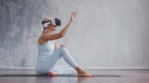 Chica joven y deportiva en ropa deportiva está haciendo ejercicios en casa utilizando casco de realidad virtual. Ajuste y delgada mujer rubia entra en los deportes y la aptitud. Salud, quemaduras de grasa y bienestar. — Vídeos de Stock