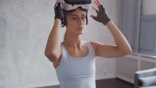 Giovane e sportiva ragazza in abbigliamento sportivo sta facendo esercizi a casa con casco realtà virtuale. In forma e snella donna bionda entra per lo sport e il fitness. Assistenza sanitaria, bruciare i grassi e benessere. — Video Stock