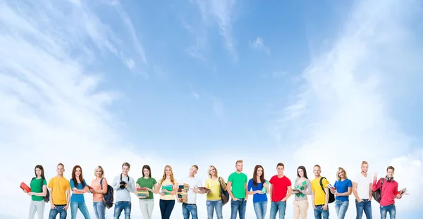 Un grande gruppo di alunni o studenti sullo sfondo del cielo. I giovani stanno davanti alla telecamera e sorridono. Istruzione e amicizia concetto. — Foto Stock