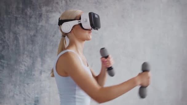 Молодая и спортивная девушка в спортивной одежде делает упражнения дома, используя шлем виртуальной реальности. Стройная блондинка занимается спортом и фитнесом. Здравоохранение, сжигание жира и оздоровление. — стоковое видео