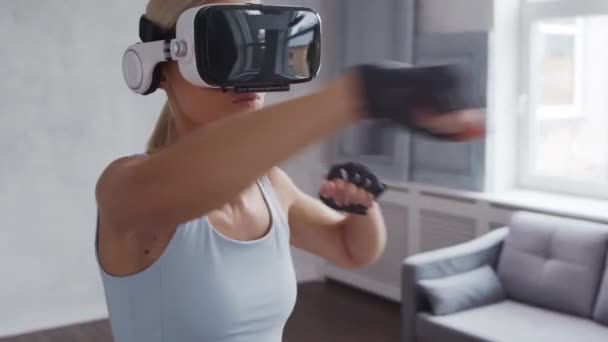 Chica joven y deportiva en ropa deportiva está haciendo ejercicios en casa utilizando casco de realidad virtual. Ajuste y delgada mujer rubia entra en los deportes y la aptitud. Salud, quemaduras de grasa y bienestar. — Vídeo de stock