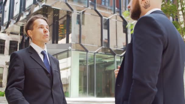 Empresário confiante e seu colega em frente ao edifício de escritórios moderno. Os investidores financeiros estão a falar ao ar livre. Banca e negócios. — Vídeo de Stock