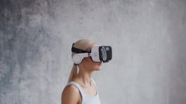 Spor giyimli genç ve sportif kız sanal gerçeklik kaskı kullanarak evde egzersiz yapıyor. Formda ve narin sarışın kadın spor ve spor için geliyor. Sağlık sigortası, yağ yakma ve sağlık..
