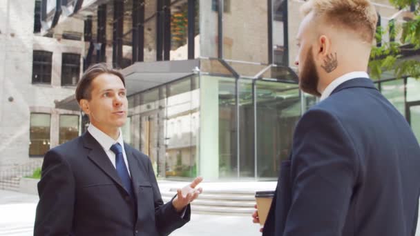 Självsäker affärsman och hans kollega framför en modern kontorsbyggnad. Finansiella investerare pratar utomhus. Banker och företag. — Stockvideo