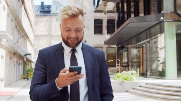Empresário confiante em frente ao edifício de escritórios moderno. investidor financeiro está usando smartphone ao ar livre. Banca e negócios. — Vídeo de Stock