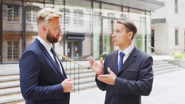 Důvěryhodný podnikatel a jeho kolega před moderní kancelářskou budovou. Finanční investoři mluví venku. Bankovnictví a obchod. — Stock video