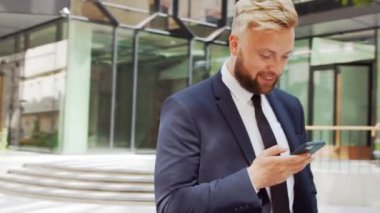 Modern ofis binasının önünde kendinden emin bir iş adamı. Finansal yatırımcı açık havada akıllı telefon kullanıyor. Bankacılık ve iş.