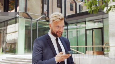 Modern ofis binasının önünde kendinden emin bir iş adamı. Finansal yatırımcı açık havada akıllı telefon kullanıyor. Bankacılık ve iş.