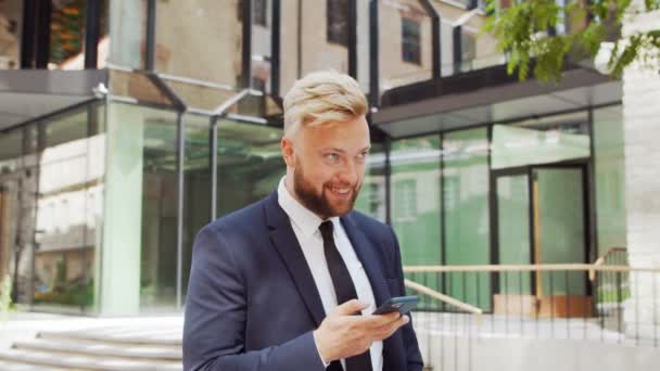 Selbstbewusster Geschäftsmann vor einem modernen Bürogebäude. Finanzinvestor setzt auf Smartphone-Outdoor Banken und Unternehmen. — Stockvideo