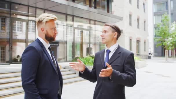 Un hombre de negocios seguro y su colega frente al moderno edificio de oficinas. Los inversores financieros están hablando al aire libre. Banca y negocios. — Vídeos de Stock