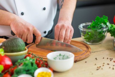 Genç aşçı modern bir mutfakta bitki ve maydanoz kesiyor. Adam evde yemek hazırlıyor. Sağlıklı ve lezzetli yemekler pişirmek..