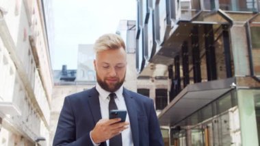 Modern ofis binasının önünde kendinden emin bir iş adamı. Finansal yatırımcı açık havada akıllı telefon kullanıyor. Bankacılık ve iş.