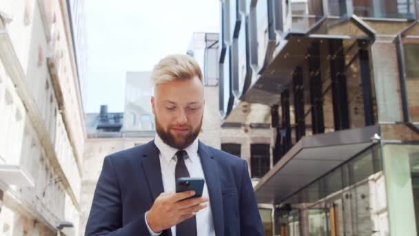 Empresário confiante em frente ao edifício de escritórios moderno. investidor financeiro está usando smartphone ao ar livre. Banca e negócios. — Vídeo de Stock