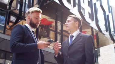 Modern ofis binasının önünde kendinden emin bir iş adamı ve meslektaşı. Finansal yatırımcılar akıllı telefon aygıtı kullanıyor ve konuşuyorlar. Bankacılık ve iş.