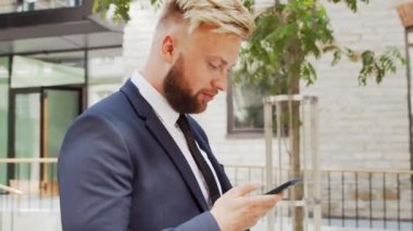 Modern ofis binasının önünde kendinden emin bir iş adamı. Finansal yatırımcı açık havada akıllı telefon kullanıyor. Bankacılık ve iş.