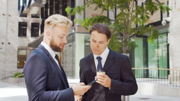 Självsäker affärsman och hans kollega framför en modern kontorsbyggnad. Finansiella investerare använder smartphone-enhet och pratar. Banker och företag. — Stockvideo